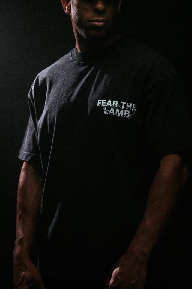 Person wearing a black t-shirt with 'FEAR THE LAMB' text on a dark background