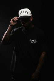 Person wearing a white cap with 'Jesus' text and a black shirt against a dark background