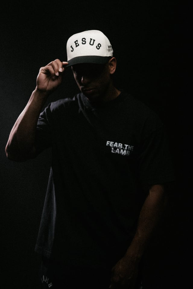 Person wearing a white cap with 'Jesus' text and a black shirt against a dark background