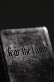 Text 'Fear the lamb' on a textured book cover with a black background