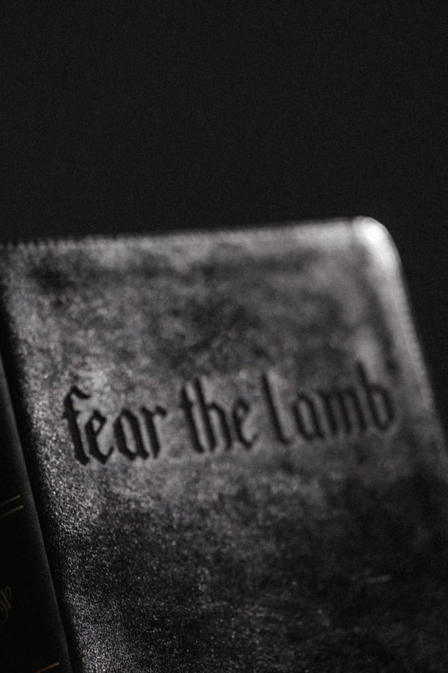 Text 'Fear the lamb' on a textured book cover with a black background