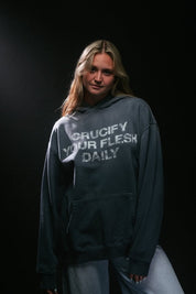 Woman wearing blue hoodie with white 'crucify your flesh daily' text on a dark background